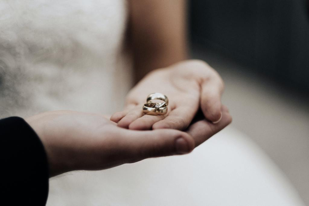 A couple's hands intertwined, showcasing an engagement ring and wedding band, symbolizing love and commitment