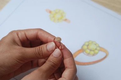 A custom-designed ring held by hands, showcasing the original sketch in the background