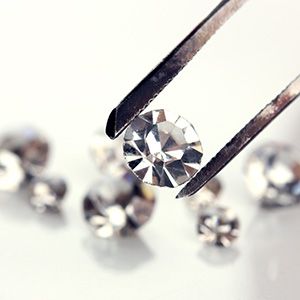 Close-up of diamond held by jeweler's tongs, surrounded by sparkling diamonds in the background